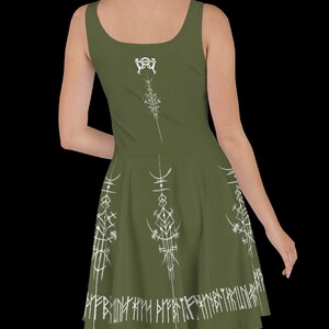 K&ouml;nnte beinhalten: Ein gr&uuml;nes, &auml;rmelloses Kleid mit einem wei&szlig;en Design aus Runen und Symbolen. Das Kleid hat einen figurbetonten Oberteil und einen ausgestellten Rock.
