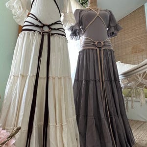May include: Two long, flowing skirts with different colored fabrics and layered ruffles. One skirt is white with a brown leather belt and the other is gray with a beige leather belt.