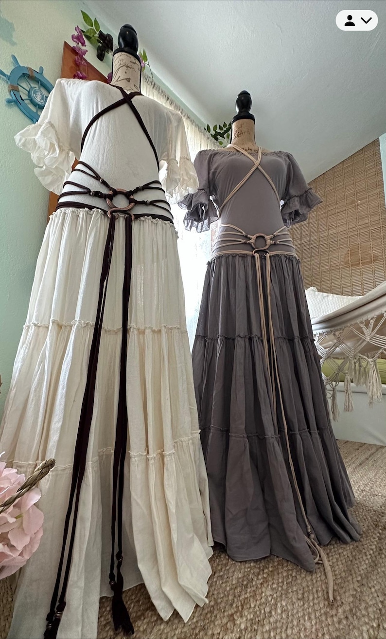 May include: Two long, flowing skirts with different colored fabrics and layered ruffles. One skirt is white with a brown leather belt and the other is gray with a beige leather belt.