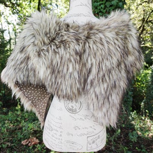 May include: A faux fur shawl in a light brown and gray color with a spotted fabric lining.
