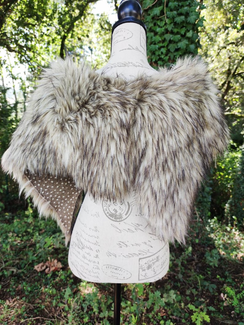 May include: A faux fur shawl in a light brown and gray color with a spotted fabric lining.