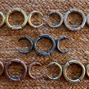 May include: Five triple moon pendants in different finishes: gold, silver, black, copper, and brass. The pendants are all the same design, with three crescent moons.