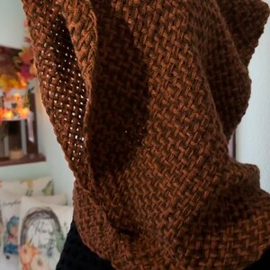 May include: A brown knitted hooded scarf with a textured pattern. The scarf is made of a soft, warm material and is perfect for keeping you warm in the winter.
