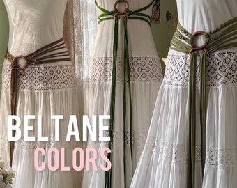 Puede incluir: Tres vestidos blancos con cinturones de diferentes colores. Los cinturones son de cuero y tienen un anillo de metal. El texto "BELTANE COLORS" está escrito en la imagen.