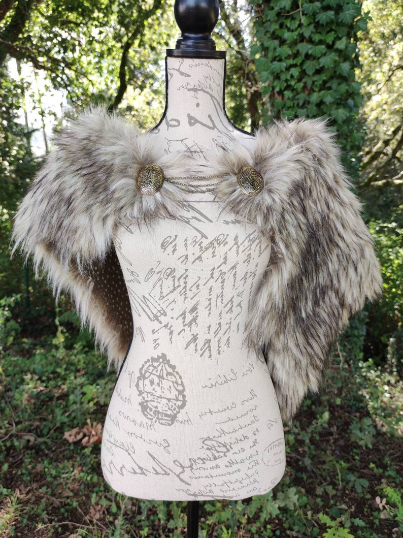 May include: A faux fur shawl with a brown and white color scheme. The shawl has two decorative metal clasps with a chain connecting them.
