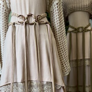 May include: A light pink dress with a crocheted lace trim and a brown leather belt with crescent moon shaped buckles and tassels.