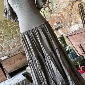 May include: A long, tiered, olive green dress with short, ruffled sleeves. The dress is made of a soft, flowing fabric and has a relaxed fit.