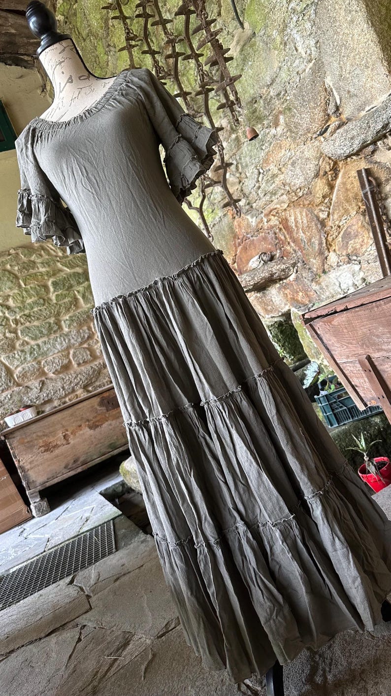 May include: A long, tiered, olive green dress with short, ruffled sleeves. The dress is made of a soft, flowing fabric and has a relaxed fit.