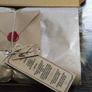 May include: A brown paper package with a brown envelope tied with twine and a red wax seal. The package is wrapped in brown tissue paper and has a tag attached with the text "Discover the magic of handmade, ethically sourced, and sustainably made goods. With love and care."