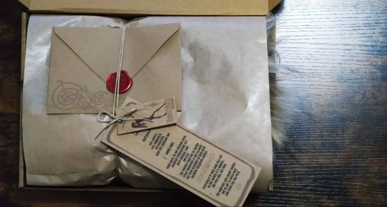 May include: A brown paper package with a brown envelope tied with twine and a red wax seal. The package is wrapped in brown tissue paper and has a tag attached with the text "Discover the magic of handmade, ethically sourced, and sustainably made goods. With love and care."