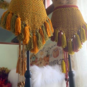 May include: Two crocheted skirts with fringe, one in shades of green and yellow, the other in shades of red and yellow. The skirts are displayed on mannequins.
