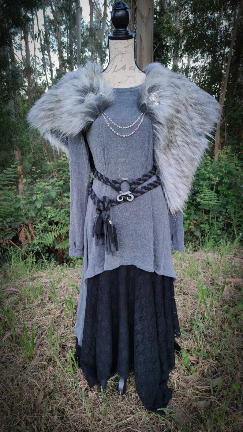 May include: A gray long-sleeved shirt with a black lace skirt and a gray faux fur collar. The shirt has a silver chain necklace and a black braided belt with a silver buckle.