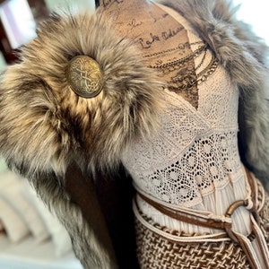 May include: A white crocheted dress with a brown woven belt and a brown fur stole with a metal clasp. The stole has a Celtic knot design.