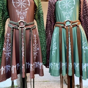 K&ouml;nnte beinhalten: Zwei braune und gr&uuml;ne Kleider mit wei&szlig;en Symbolen und Runen. Die Kleider haben braune Lederg&uuml;rtel mit Quasten. Die Kleider befinden sich auf Mannequins mit braunen und gr&uuml;nen H&auml;kel-Oberteilen.