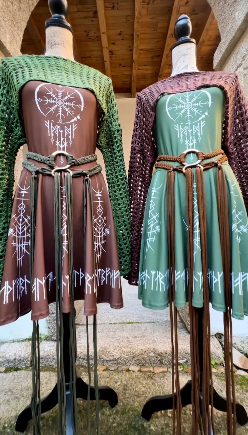 K&ouml;nnte beinhalten: Zwei braune und gr&uuml;ne Kleider mit wei&szlig;en Symbolen und Runen. Die Kleider haben braune Lederg&uuml;rtel mit Quasten. Die Kleider befinden sich auf Mannequins mit braunen und gr&uuml;nen H&auml;kel-Oberteilen.