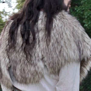 May include: A white and gray faux fur collar with a long, dark brown hairpiece. The collar is worn around the neck and shoulders.