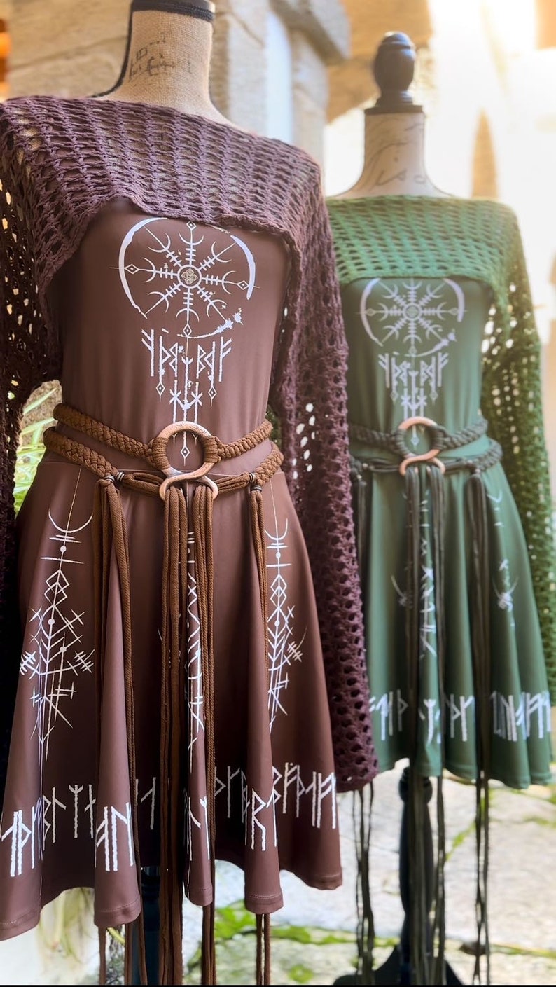K&ouml;nnte beinhalten: Zwei braune und gr&uuml;ne Kleider mit einem wei&szlig;en geometrischen Muster und einem braunen geflochtenen G&uuml;rtel mit einem gro&szlig;en Metallring. Die Kleider haben einen H&auml;kel&uuml;berzug.