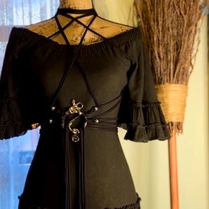 May include: A black off-the-shoulder dress with a gold snake-shaped belt and a black choker necklace. The dress has a ruffled hem and sleeves.