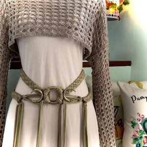 May include: A beige crochet top with long sleeves and a matching belt with a large, silver, crescent moon buckle. The belt has long, thin tassels.