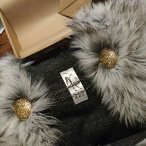 May include: A gray faux fur collar with a gray fabric lining and two gold metal clasps. The collar has a tag with the text "Stark Industries" and a chain attached to the clasps.