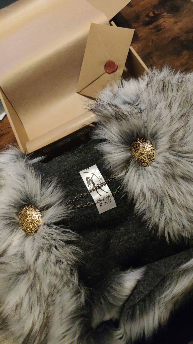 May include: A gray faux fur collar with a gray fabric lining and two gold metal clasps. The collar has a tag with the text "Stark Industries" and a chain attached to the clasps.