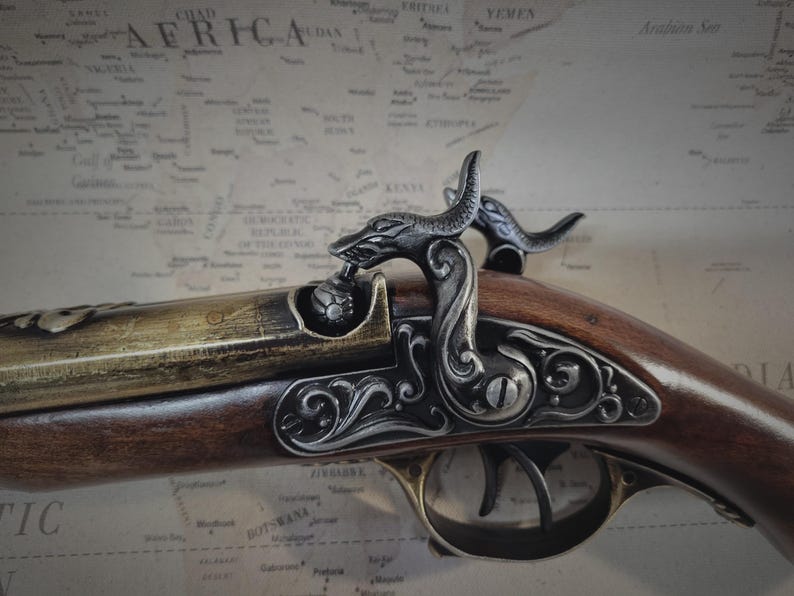 May include: A detailed, ornate, black and gold pistol with a wooden stock and a decorative, sculpted, dragon-like handle.
