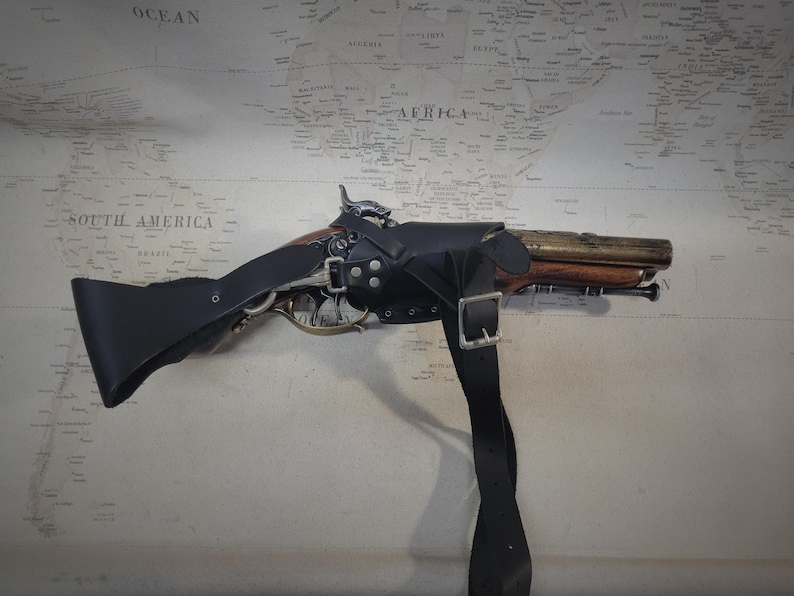 May include: A black leather holster with a strap for a flintlock pistol. The pistol is made of wood and metal and has a brass barrel.