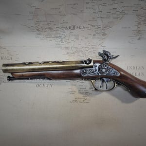 May include: A decorative, antique-style, brass and wood pistol with intricate carvings and a skull and crossbones on the handle. The pistol is lying on a map of the world.