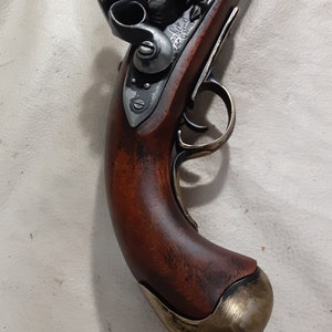 Op de afbeelding: Een antiek-stijl flintlock pistool met een houten handvat. Het pistool heeft een messing loopband en een messing trekkerbeugel. Het pistool is in goede staat en heeft een donkerbruine afwerking.