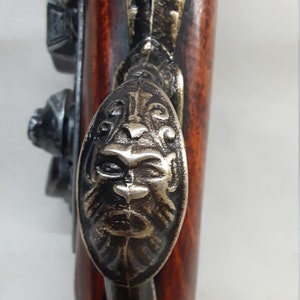 May include: A close-up of a decorative, ornate, metal handle on a wooden gun. The handle is shaped like a lion's head and has a detailed design.