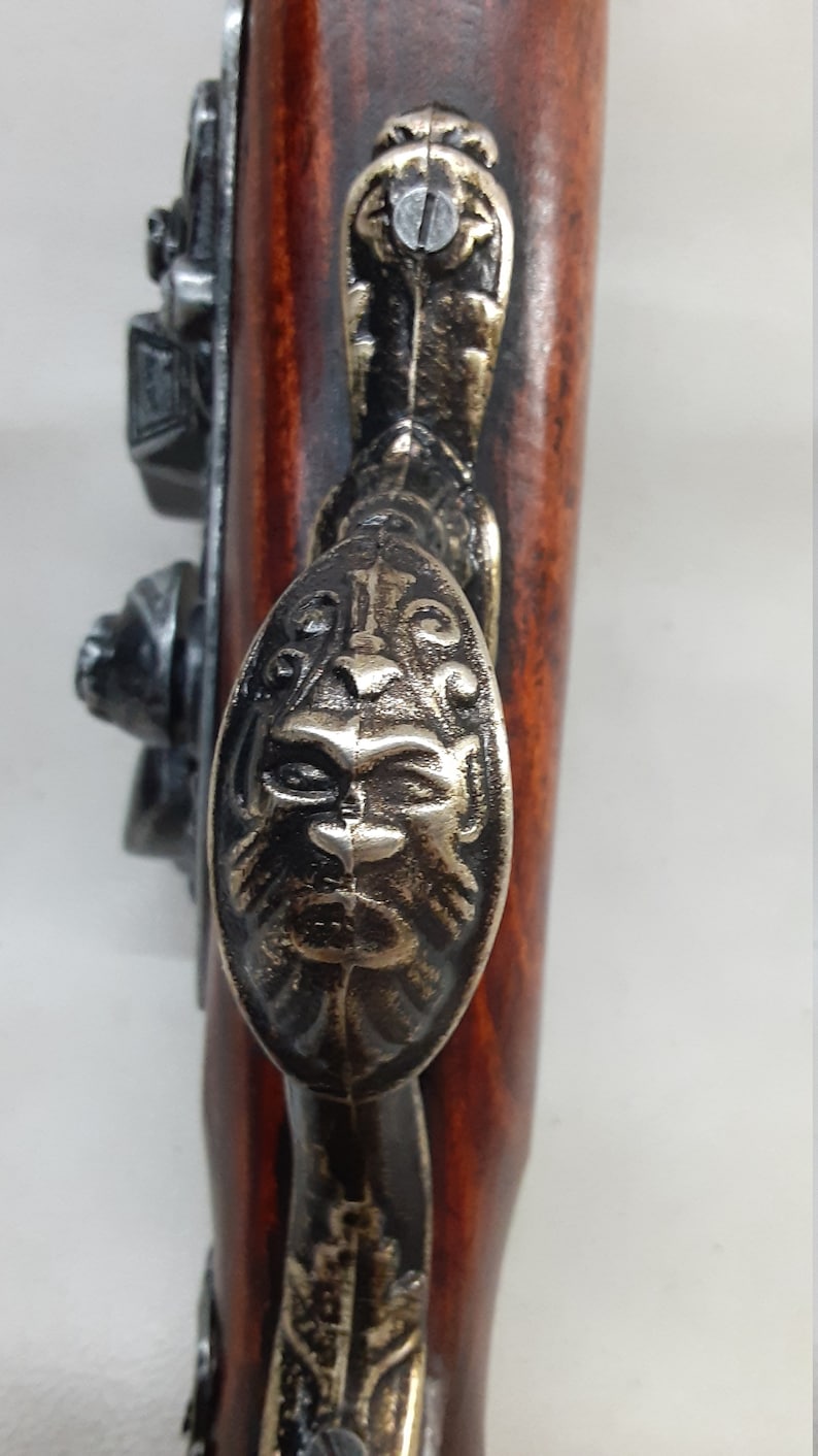 May include: A close-up of a decorative, ornate, metal handle on a wooden gun. The handle is shaped like a lion's head and has a detailed design.