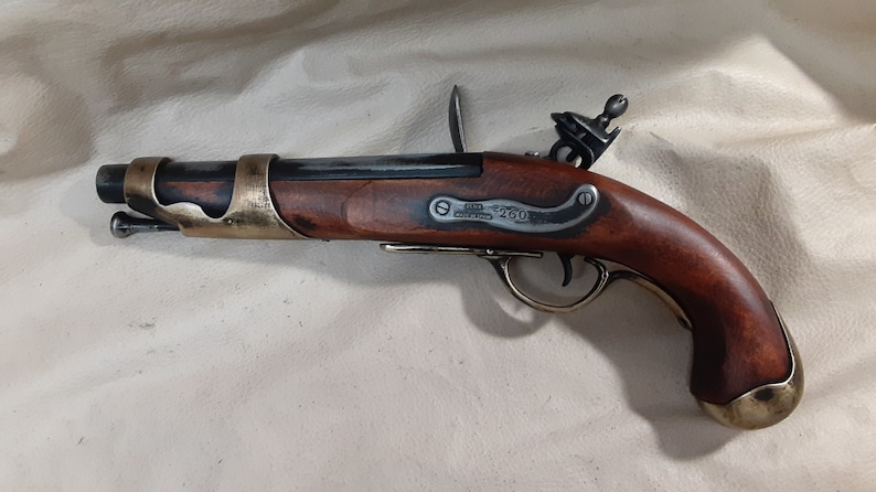 Op de afbeelding: Een zwart en messing vuursteenpistool met een houten handvat. Het pistool heeft een messing trekkerbeschermer en een messing loopband. Het pistool is gegraveerd met de tekst "J.M.  LONDON  260".