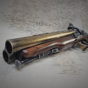 May include: A gold and brown antique-style triple-barreled pistol with a wooden handle and intricate metalwork.
