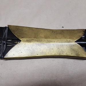 May include: A close-up of a black and gold sword with a decorative handle. The handle is wrapped in black wire and has a gold metal tip.