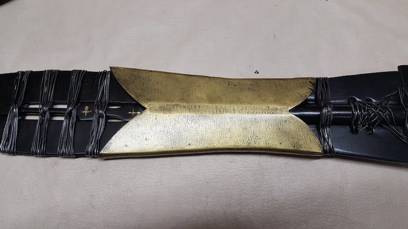 May include: A close-up of a black and gold sword with a decorative handle. The handle is wrapped in black wire and has a gold metal tip.