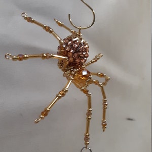 May include: A gold beaded spider ornament with a crystal teardrop hanging from one leg. The spider has a round body and eight legs.