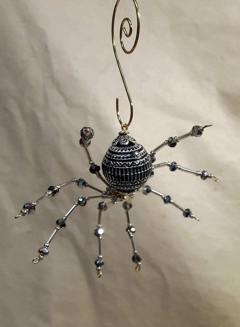 May include: A black and silver beaded spider ornament with a gold wire hanger. The spider's body is a round, black bead with silver accents.