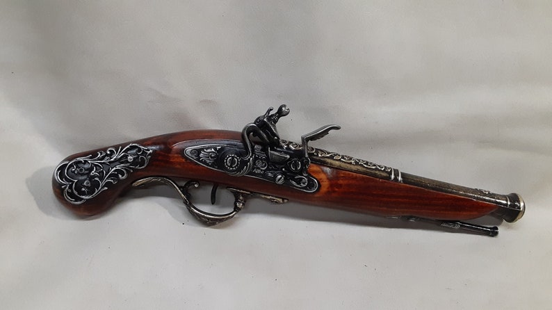 May include: A decorative antique-style flintlock pistol with a wooden handle and metal accents. The handle is intricately carved with floral designs.