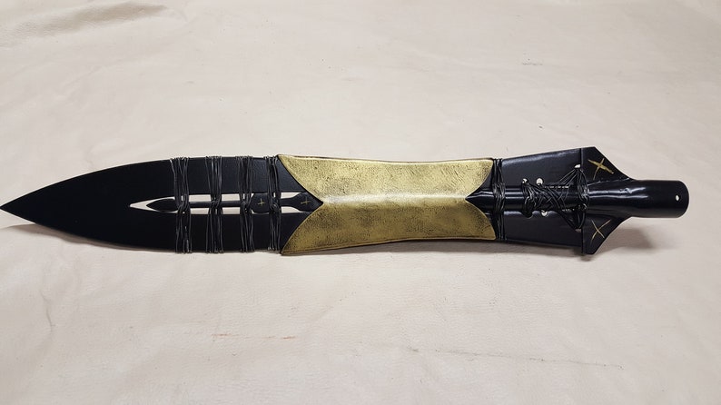 May include: A black and gold spear with a leather wrap and decorative details. The spear has a sharp point and a wooden handle.