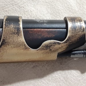 Op de afbeelding: Een close-up van een zwart en bruin houten pistool met een gouden metalen accent. Het pistool heeft een zwarte metalen loop en een houten handvat.