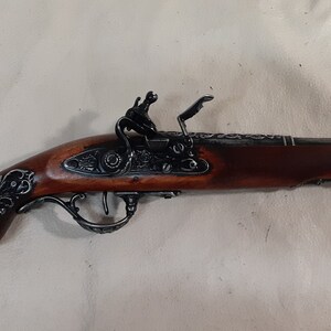 May include: A silver and brown decorative flintlock pistol with intricate floral engravings on the handle and barrel. The pistol has a wooden grip and a metal trigger guard.