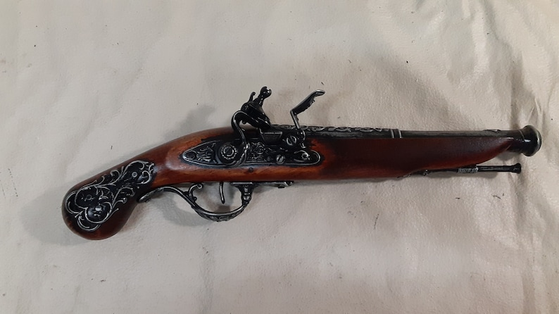 May include: A silver and brown decorative flintlock pistol with intricate floral engravings on the handle and barrel. The pistol has a wooden grip and a metal trigger guard.