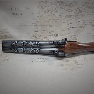 May include: A silver and brown double-barreled pistol with intricate skull and floral engravings. The pistol has a wooden handle and a metal barrel.