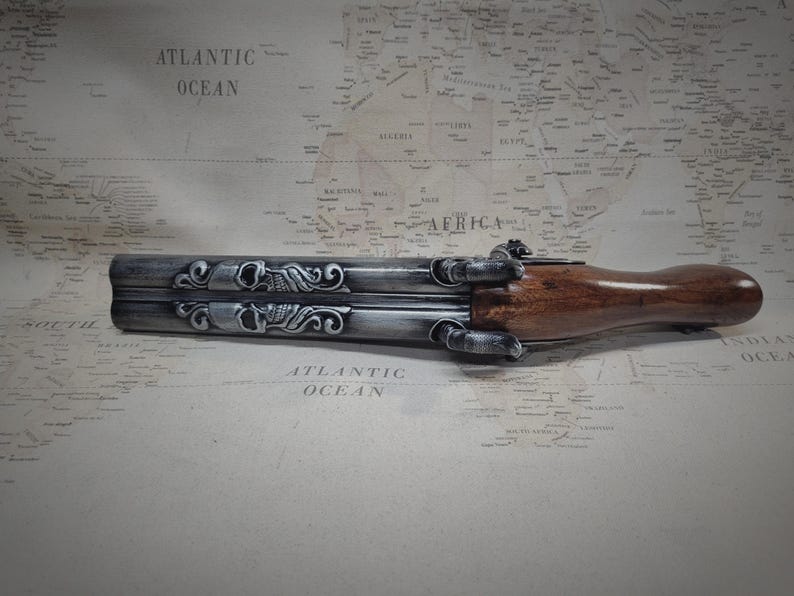 May include: A silver and brown double-barreled pistol with intricate skull and floral engravings. The pistol has a wooden handle and a metal barrel.