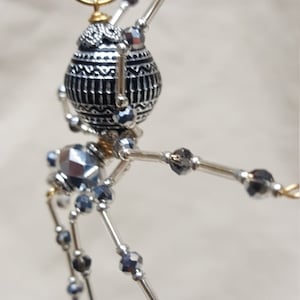 May include: A silver and black beaded spider ornament with a patterned sphere body and a gold wire hanger.