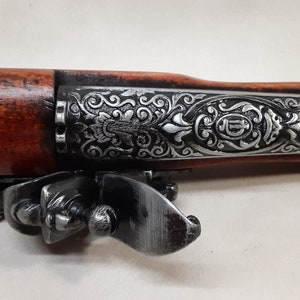 May include: A decorative, silver-plated pistol with a wooden handle and intricate floral engravings. The pistol has a trigger guard and a hammer.