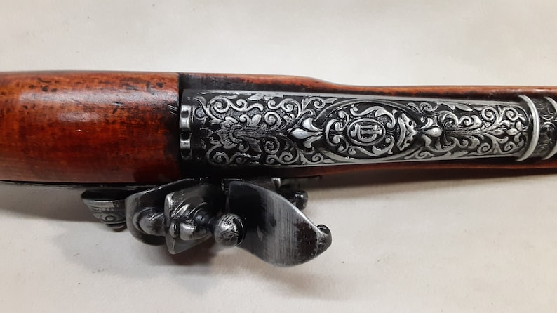 May include: A decorative, silver-plated pistol with a wooden handle and intricate floral engravings. The pistol has a trigger guard and a hammer.