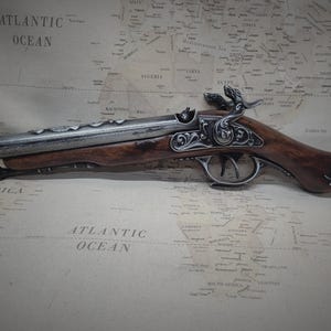 May include: A silver and brown pirate pistol with intricate details and a skull and crossbones design on the handle. The pistol is lying on a vintage world map.