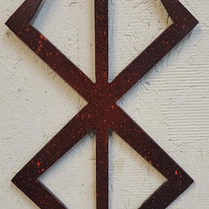 May include: A dark red, geometric symbol with a speckled texture. The design features a central vertical line with a three-pronged top and intersecting diagonal lines, forming a diamond shape. The symbol is set against a textured white background.