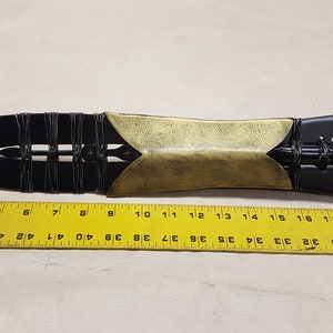 May include: A black and gold spearhead with a leather wrap. The spearhead is about 20 inches long and is measured against a ruler.